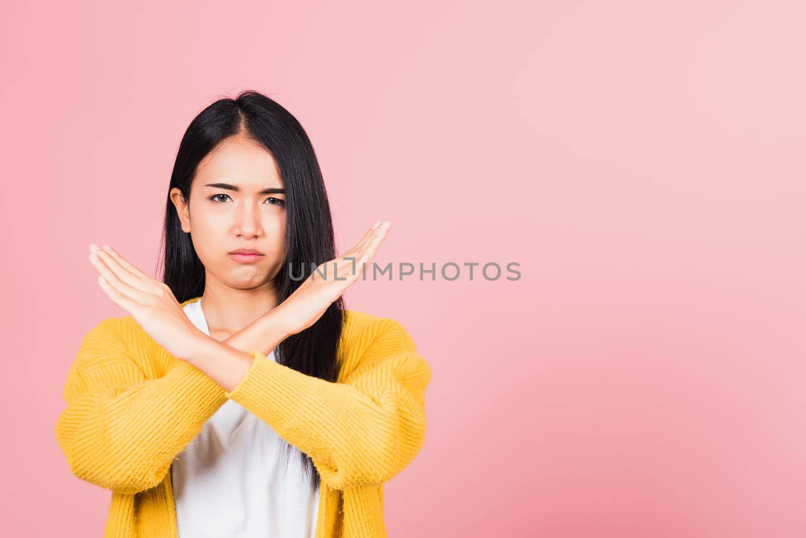 Portrait Asian beautiful young woman unhappy or confident standing wear holding two cross arms say no X sign, studio shot isolated pink background, Thai female pose reject gesture with copy space