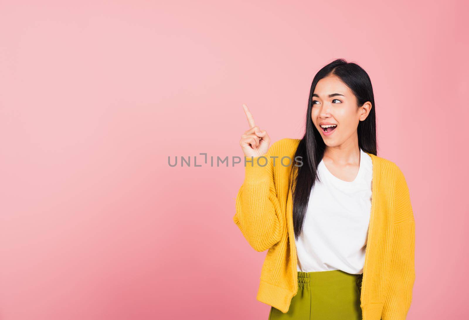 Portrait Asian beautiful young woman smiling standing pointing finger out on pink background, Thai happy face excited female point into empty looking to side away with copy space for text