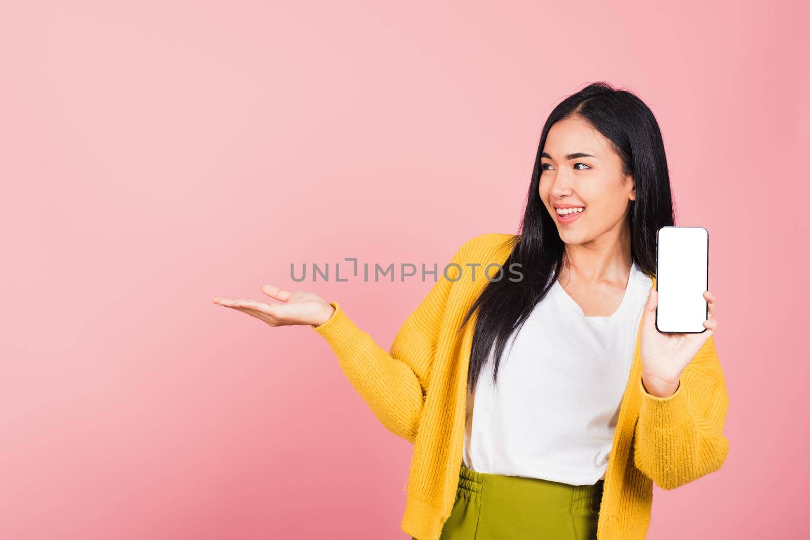 Happy Asian portrait beautiful cute young woman excited holding mobile phone blank screen presenting product with palm of hand at empty, studio shot isolated on pink background, female look to space