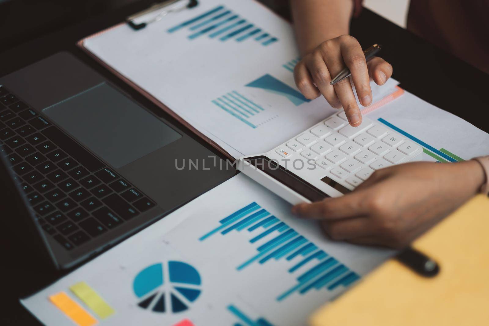 Above view of accouting woman consultant holding pen and using calculator with financial report on wooden desk at home. freelance, tax, accounting, statistics and analytic research concept.