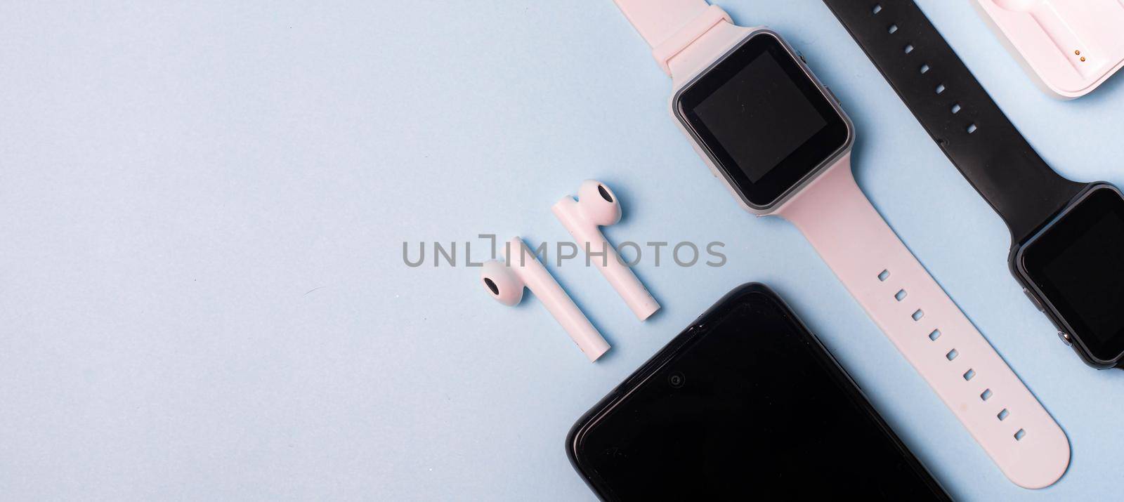 The layout of the watch and the phone on a blue background. Appliances and electronics. Modern gadgets. Phone headphones watch. Business. Student. Wireless headphone. Watch with pedometer. Copy space