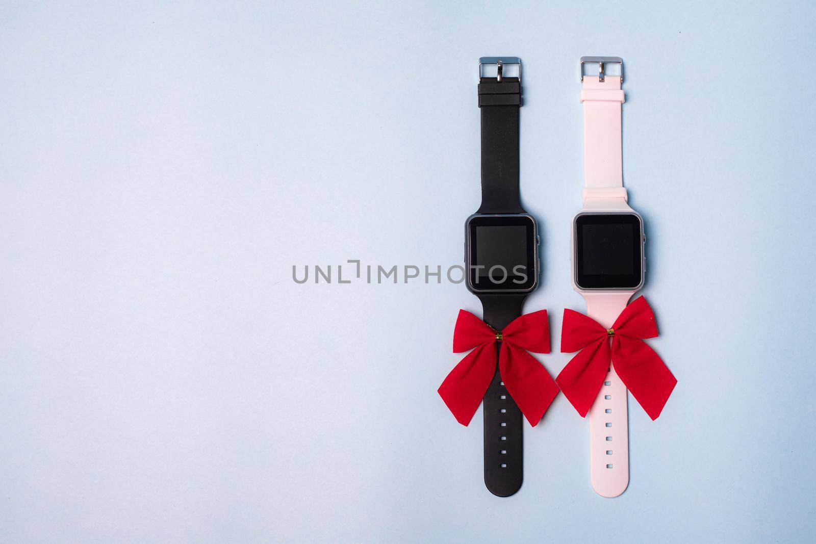 The watch is white and black electronic with a bow on a plain background . The watch is handmade with a bow . Gift watch is white with a red bow on a blue background. Modern watches. Pedometer. A gift for the holiday. Blue background. Watch as a gift