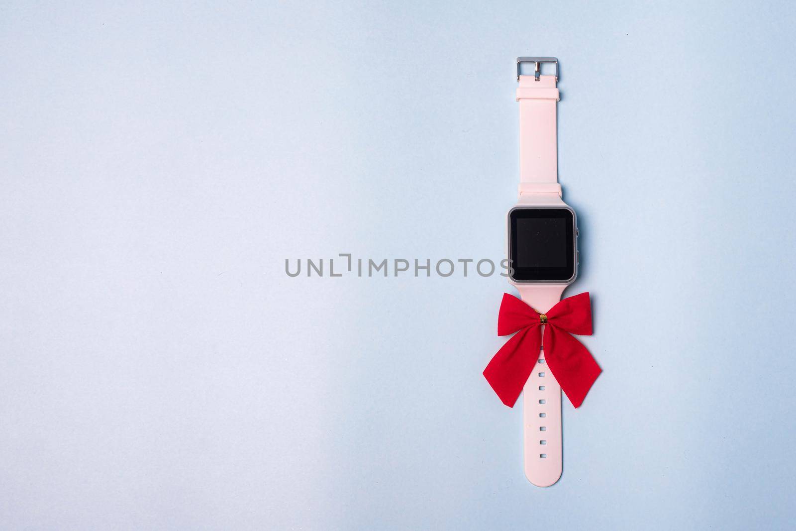 White electronic watch with a bow on a plain background . The watch is handmade with a bow . Gift watch is white with a red bow on a blue background. Modern watches. Pedometer. A gift for the holiday. Blue background. Watch as a gift