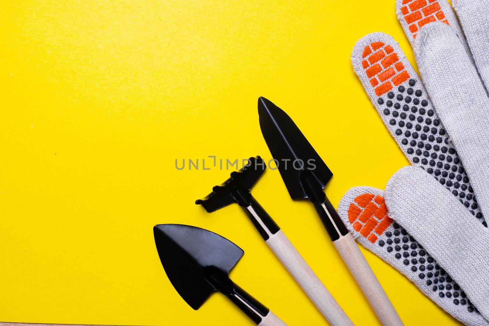 Gardening layout on a yellow background . Gardening gloves and flower shovels. Spring season. Plantings. Landings in the ground. Copy space.