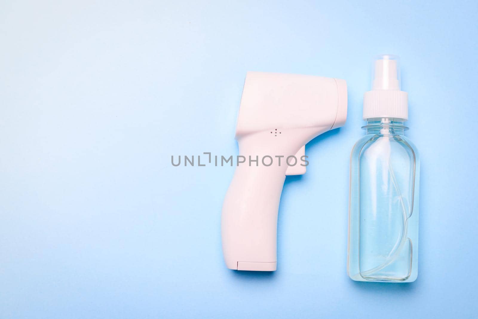 infrared thermometer and antiseptic on a blue background . antiseptic. treatment of hands. prevention. non-contact temperature measurement. health. coronavirus. pandemic. human health. check the temperature. copy space