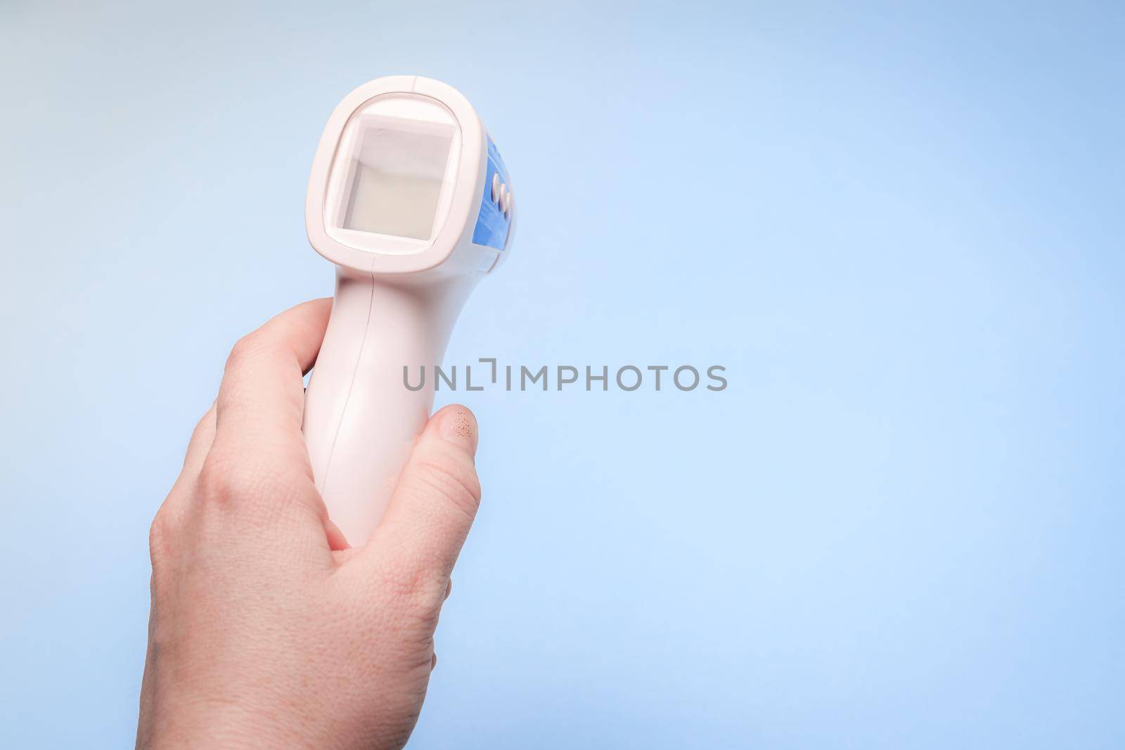 infrared thermometer on a blue background in your hand. the thermometer in his hand . prevention. non-contact temperature measurement. health. coronavirus. pandemic. human health. check the temperature. copy space