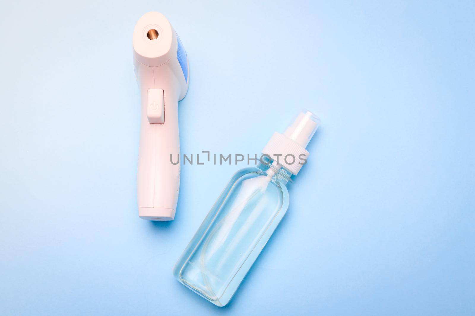 infrared thermometer and antiseptic on a blue background . antiseptic. treatment of hands. prevention. non-contact temperature measurement. health. coronavirus. pandemic. human health. check the temperature. copy space