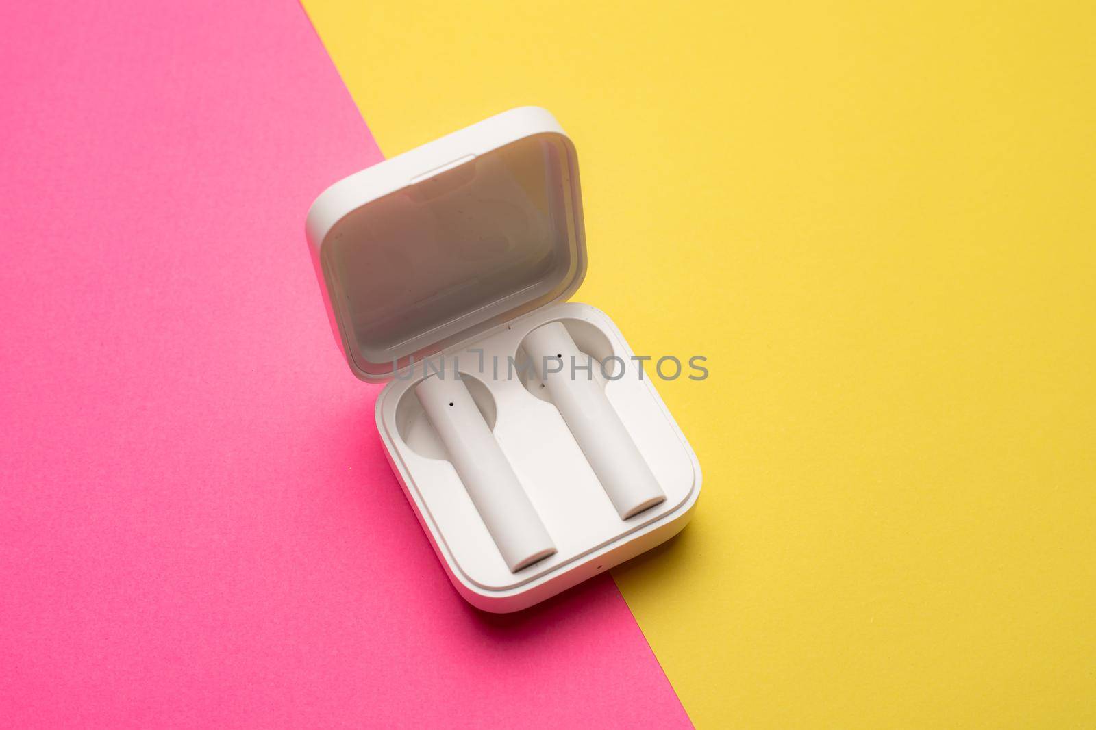 Wireless headphones on a pink background . Bright background. White headphones. Bluetooth headset. Pink and yellow background. Copy space. An article about technology. Modern technologies.