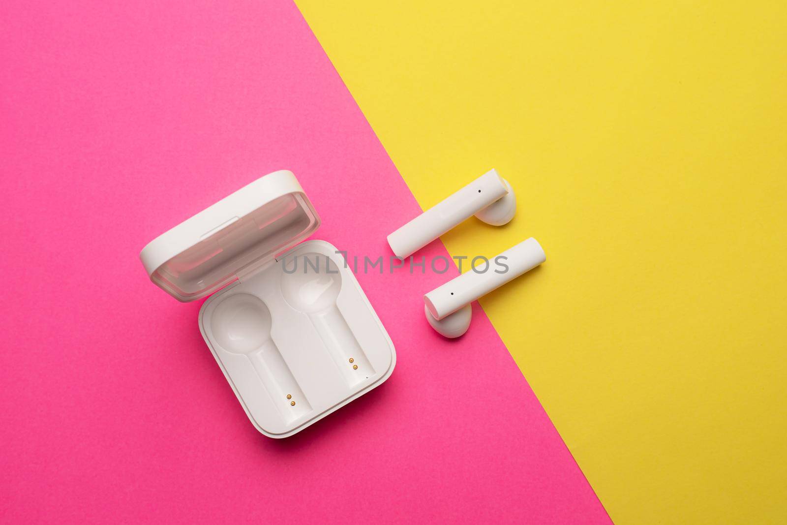 Wireless headphones on a pink background . Bright background. White headphones. Bluetooth headset. Pink and yellow background. Copy space. An article about technology. Modern technologies.
