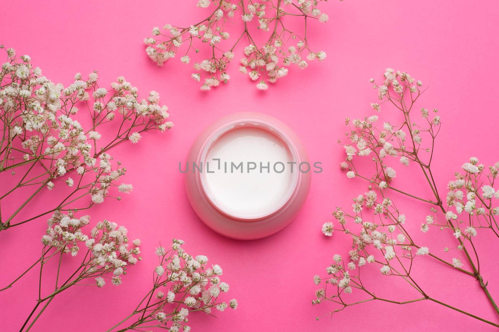 Cream for face in flowers . Face cream on a pink background. Skin care. The beauty industry. Copy space. White flowers. Article about the right choice of cream. Selection of the cream. Spa treatments. Cosmetology.