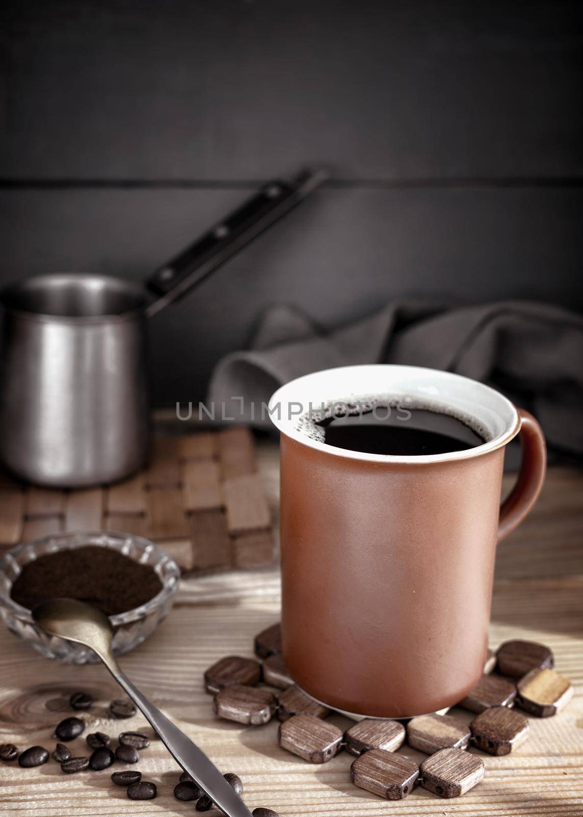 On the table on a napkin is a Cup of black coffee, next to coffee beans, ground coffee. Front view, close-up. Copy space