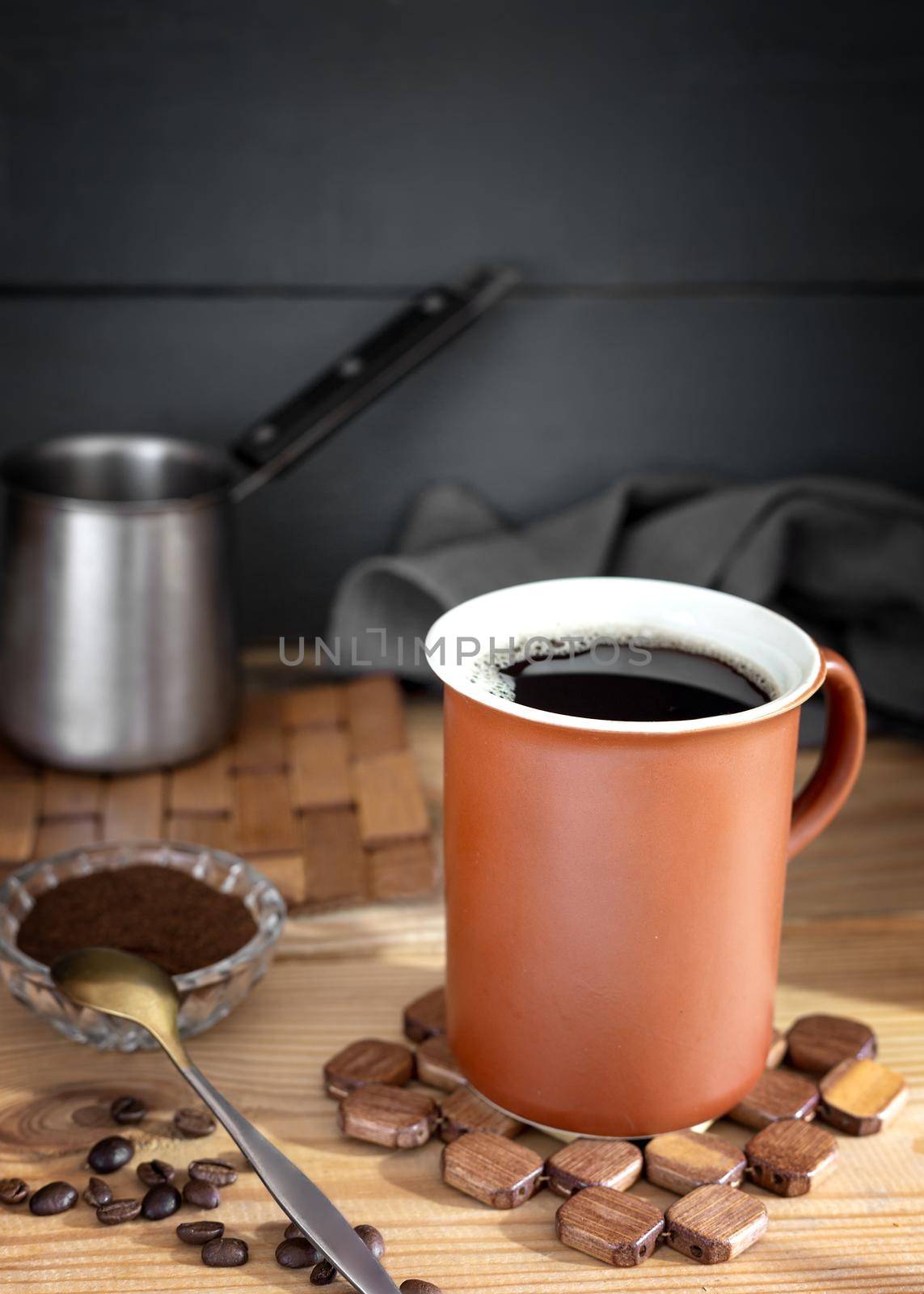 On the table on a napkin is a Cup of black coffee, next to coffee beans, ground coffee. Front view, close-up. Copy space