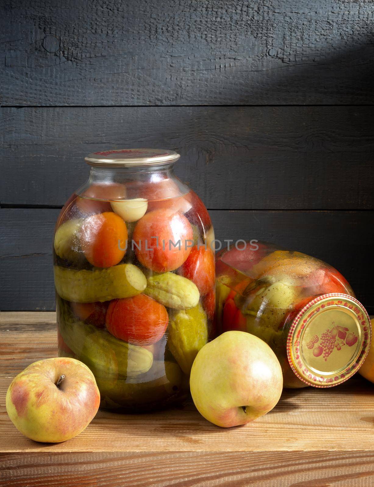 On a shelf in the basement are two glass jars with canned tomatoes, cucumbers, and peppers. Sealed with a sealed lid. Front view, copy space.