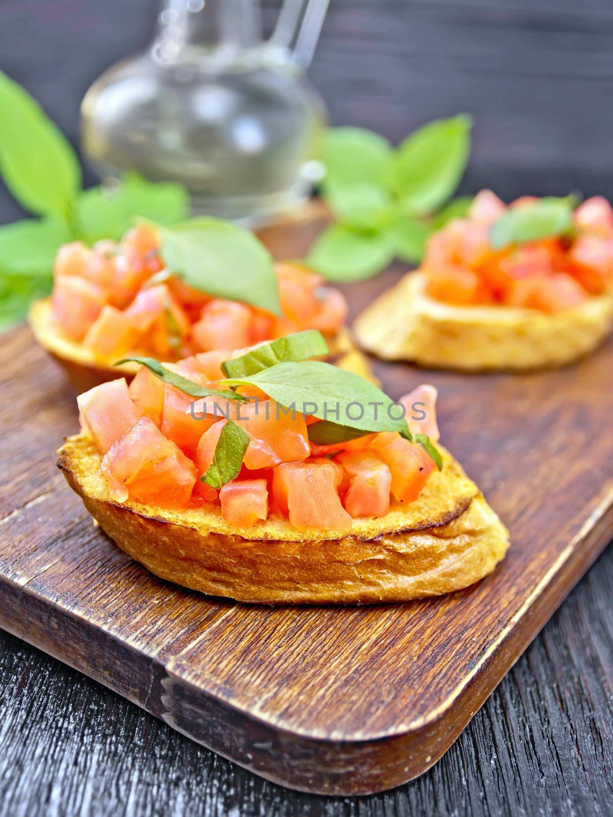 Bruschetta with tomatoes and basil, vegetable oil in a decanter on a wooden board background