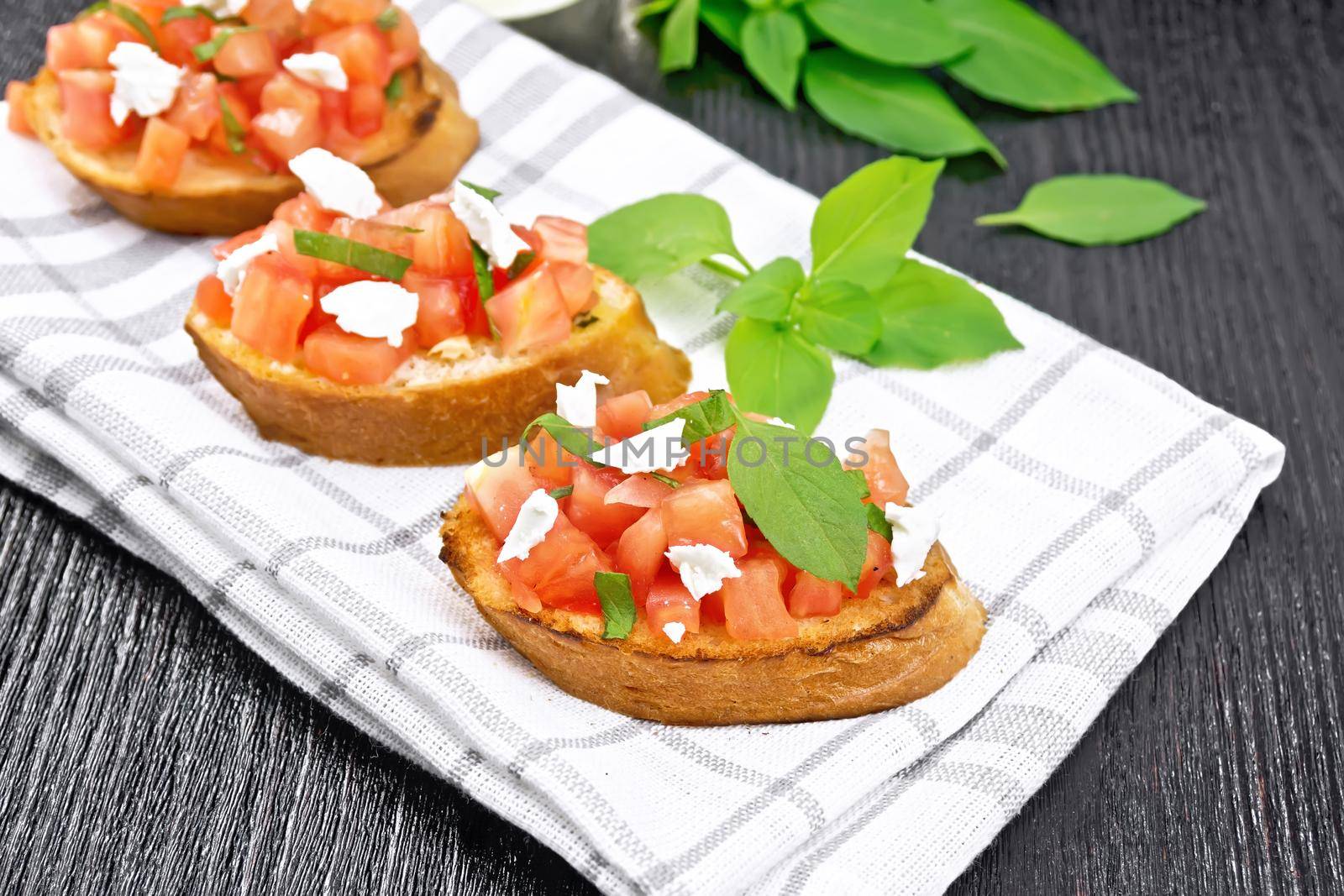Bruschetta with tomato, basil and soft cheese on a towel on dark wooden board