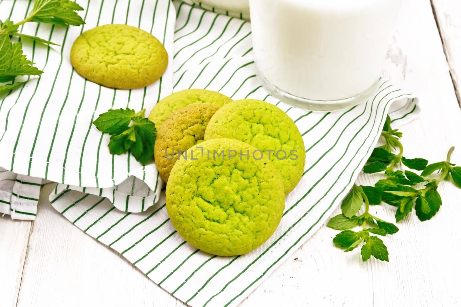 Green mint cookies on a towel with milk in a glass on wooden board background