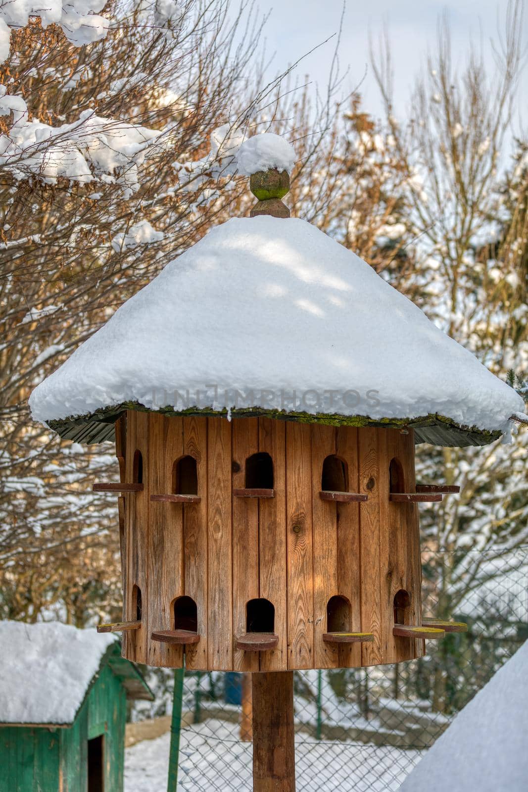 Wooden Dovecote with a roof cowered by snow, a house for pigeons made of wood in the garden as a nest for birds.