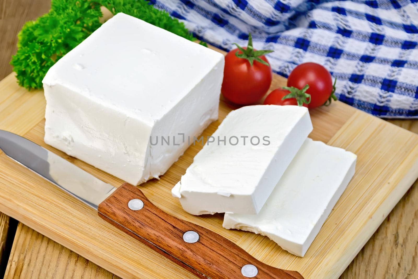 White brine cheese, knife, parsley, tomatoes, napkin on a wooden boards background