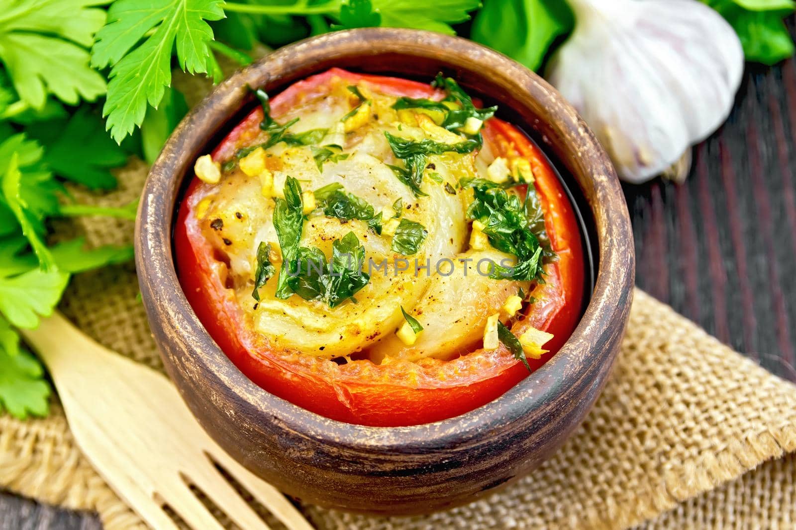 Fish baked in tomato in Zandvoort in clay bowl on a napkin of burlap, parsley and fork on the background of wooden boards