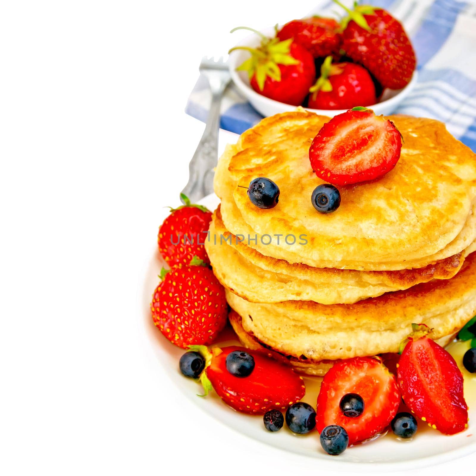 A stack of pancakes with strawberries, blueberries, honey on a white plate, fork, napkin isolated on white background