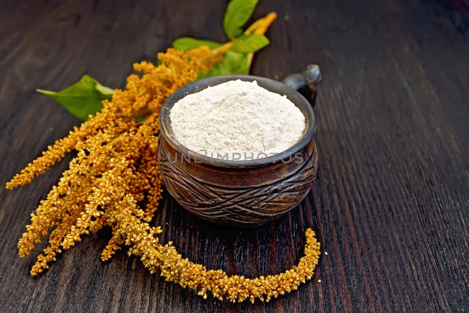 Flour amaranth in a clay cup, brown flower with green leaves on a background of wooden boards
