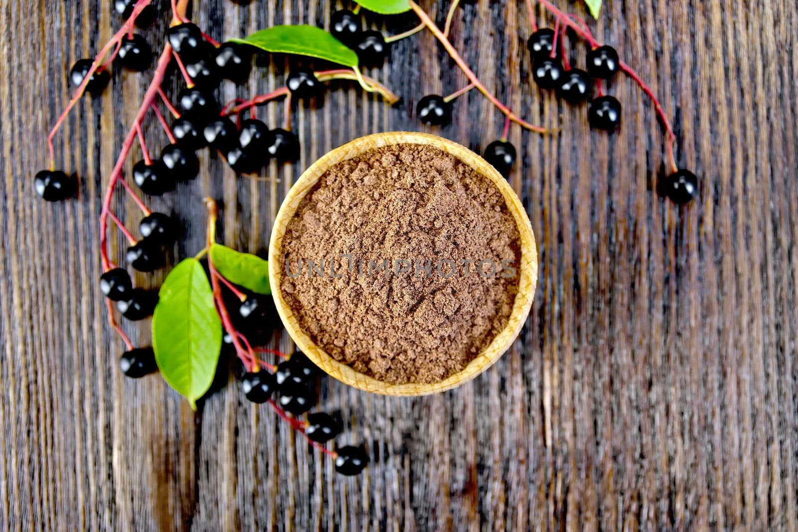 Flour of bird-cherry in a bowl with berries on a background of wooden boards top