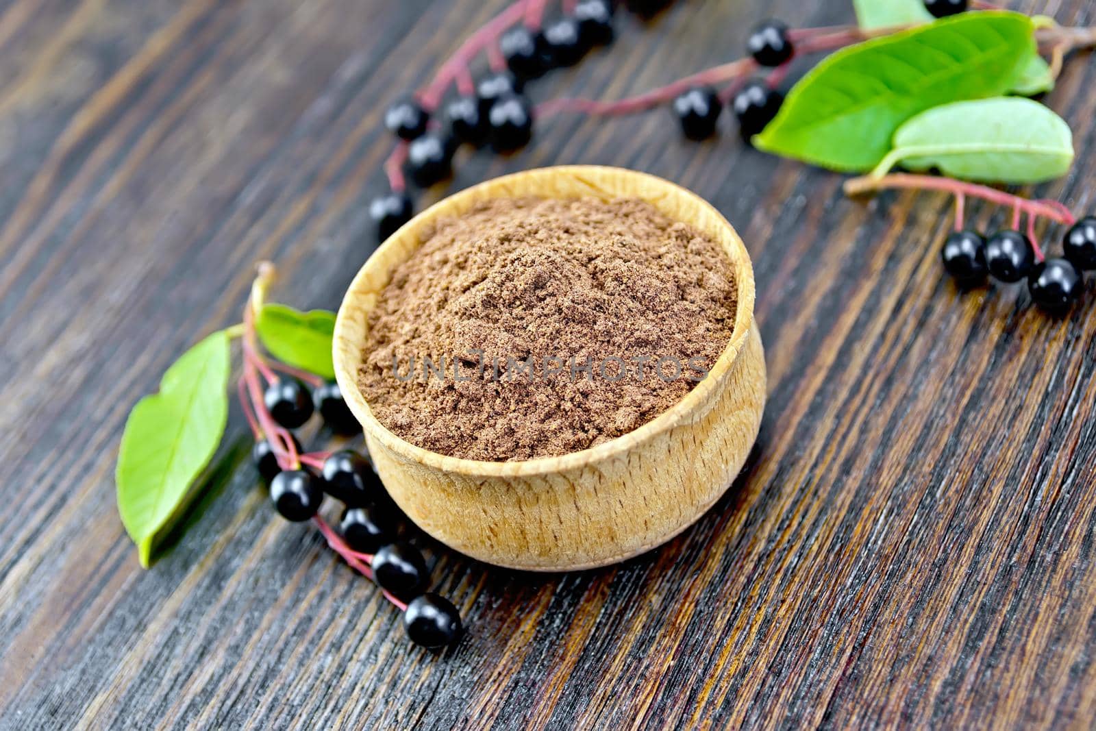 Flour of bird-cherry in a bowl with black berries on a background of wooden boards