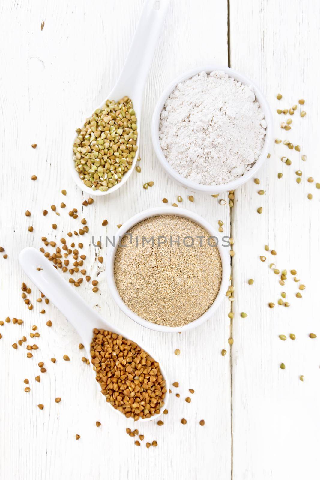 Buckwheat flour from brown and green cereals in two bowls, spoons with different buckwheat groats on the background of light wooden board from above