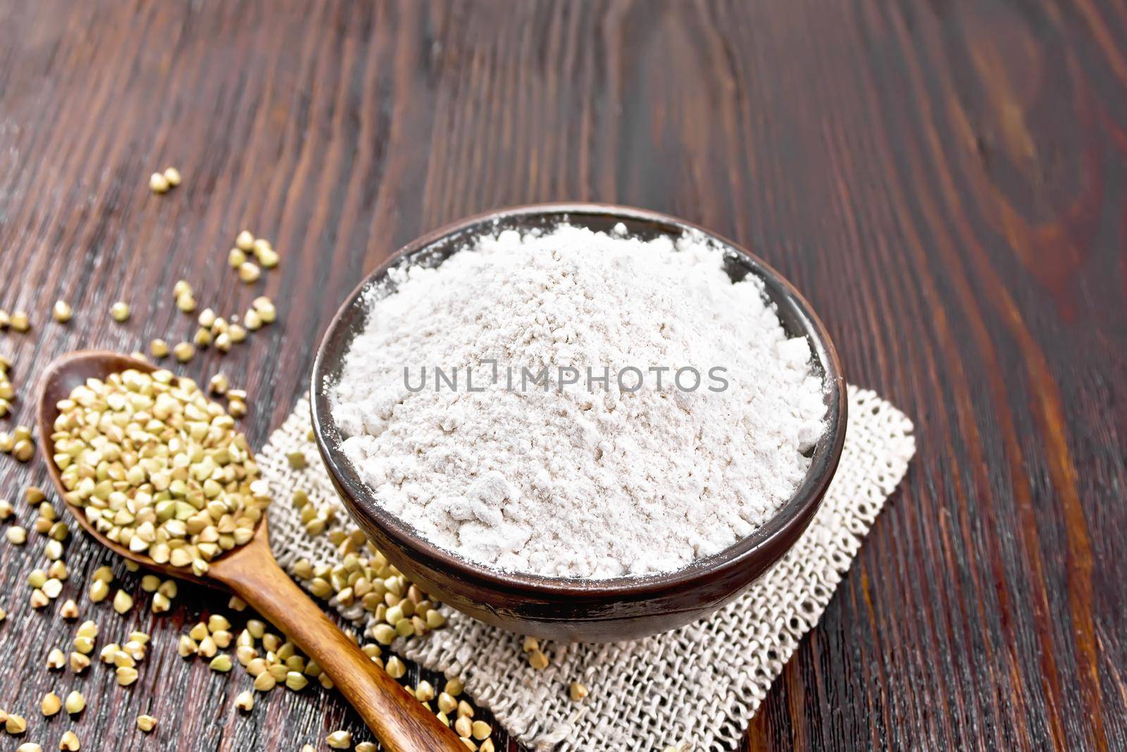 Buckwheat flour from green cereals in a bowl on sacking, groats in spoons and on a table against background of wooden board