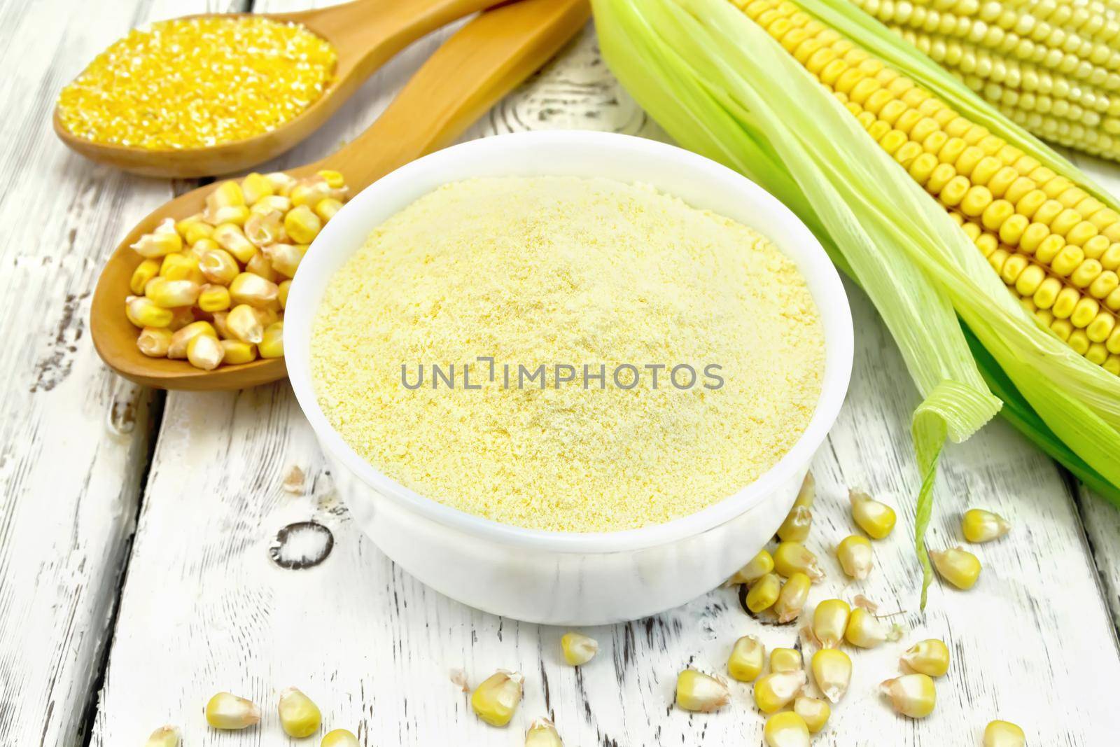 Flour corn in a bowl, groats and grain maize in the spoons, cobs on the background of wooden boards