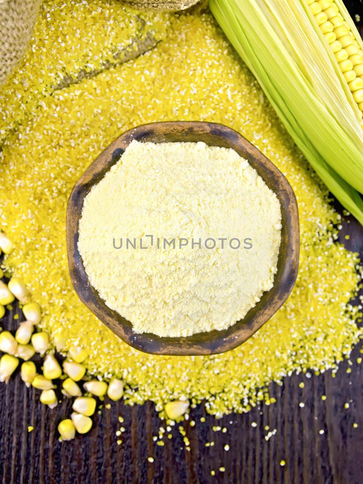 Flour corn in a clay bowl on the grits, cobs and grains, a sack on the background of the wooden planks on top