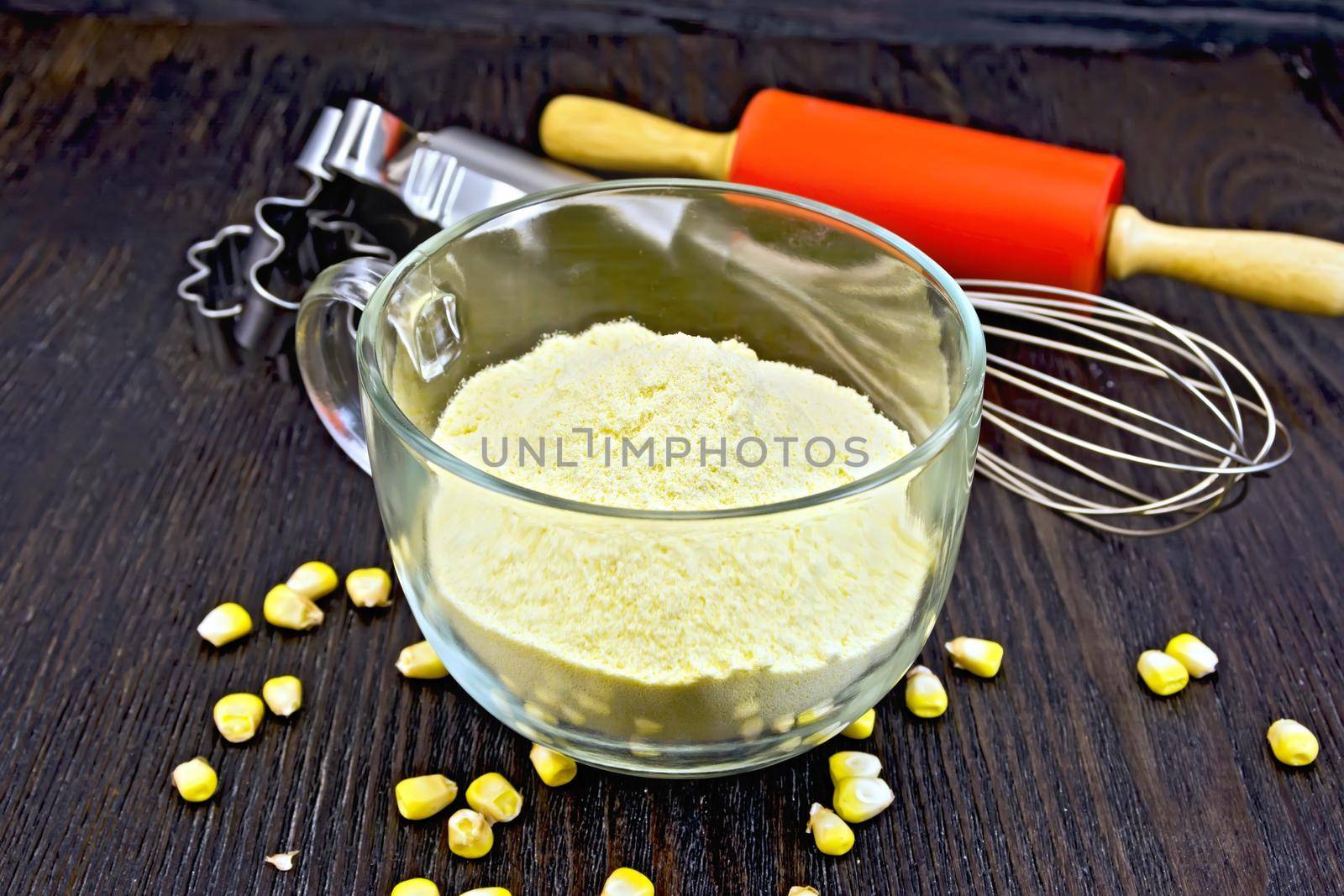 Flour corn in cup, grain, rolling pin and metal cookie cutters on a wooden board