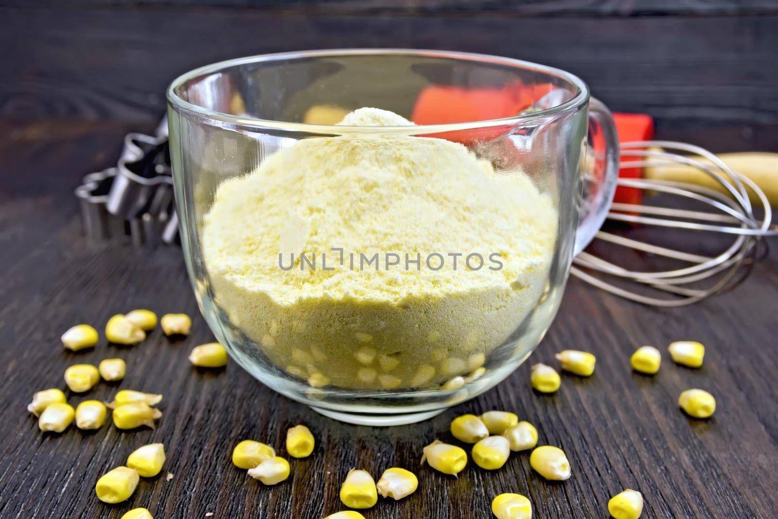 Flour corn in a glass cup, grain, rolling pin on a wooden boards background