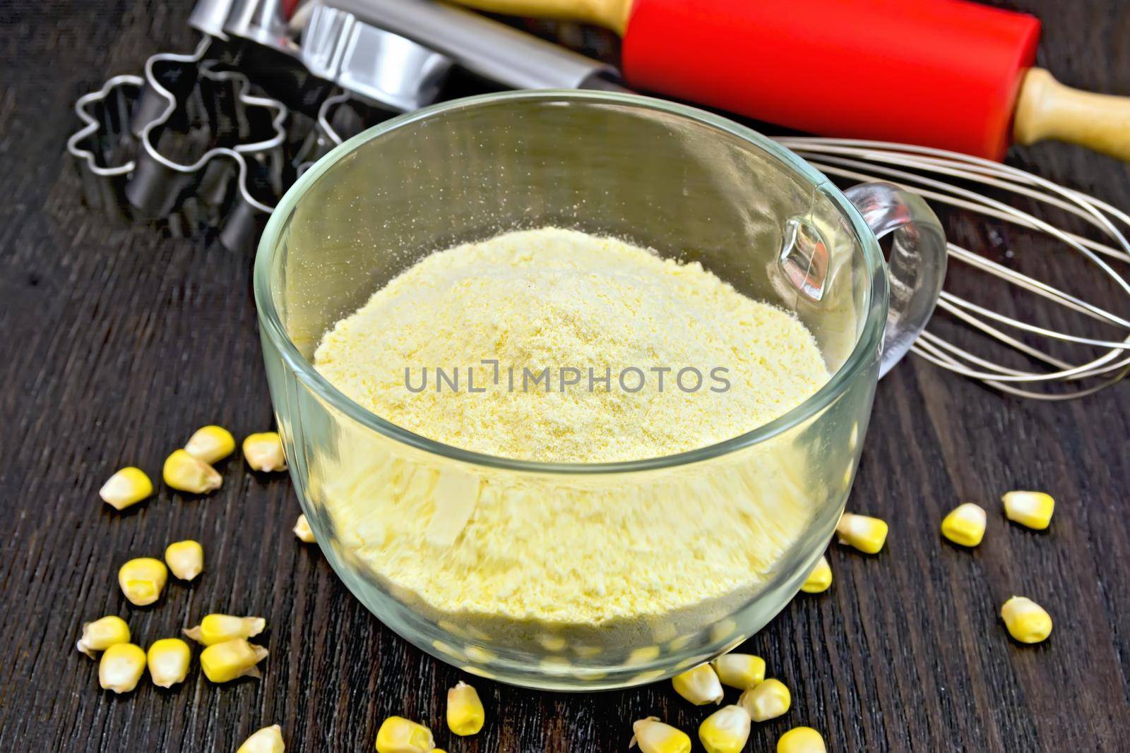 Flour corn in a glass cup, grain, rolling pin and metal cookie cutters on a wooden board