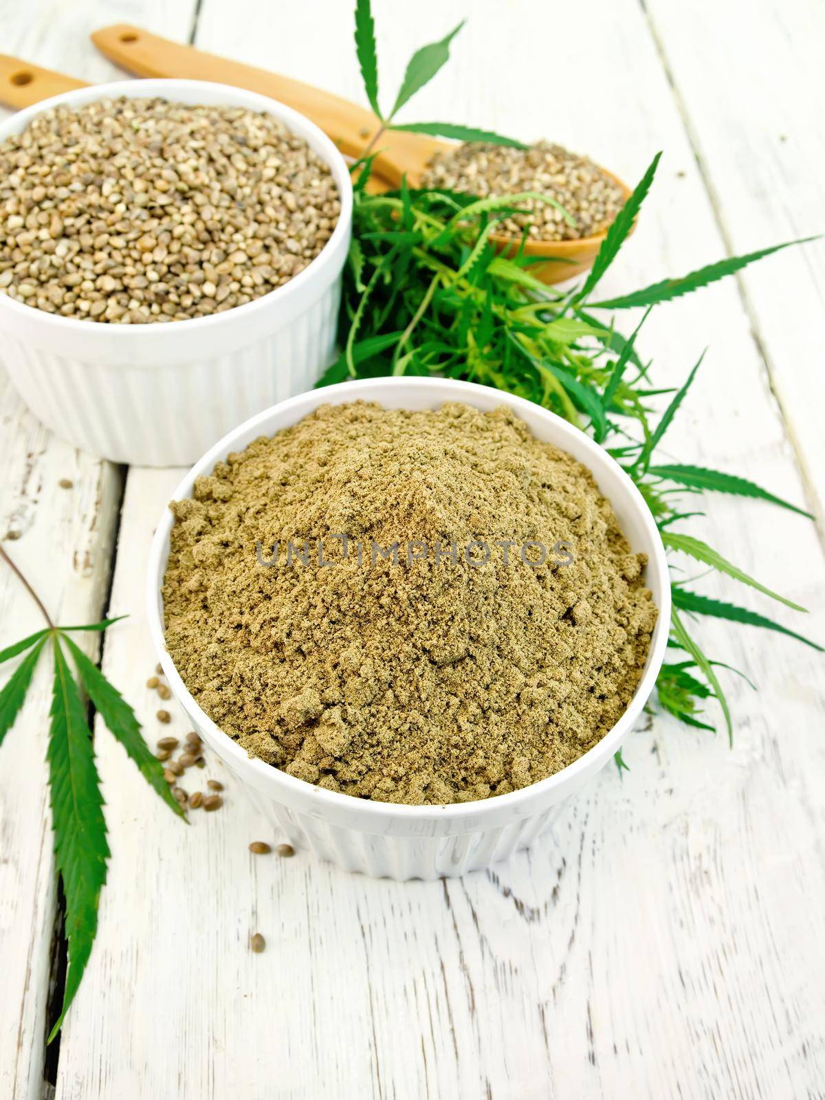 Flour and hemp grain in white bowl and spoon, cannabis leaves on the background of wooden boards