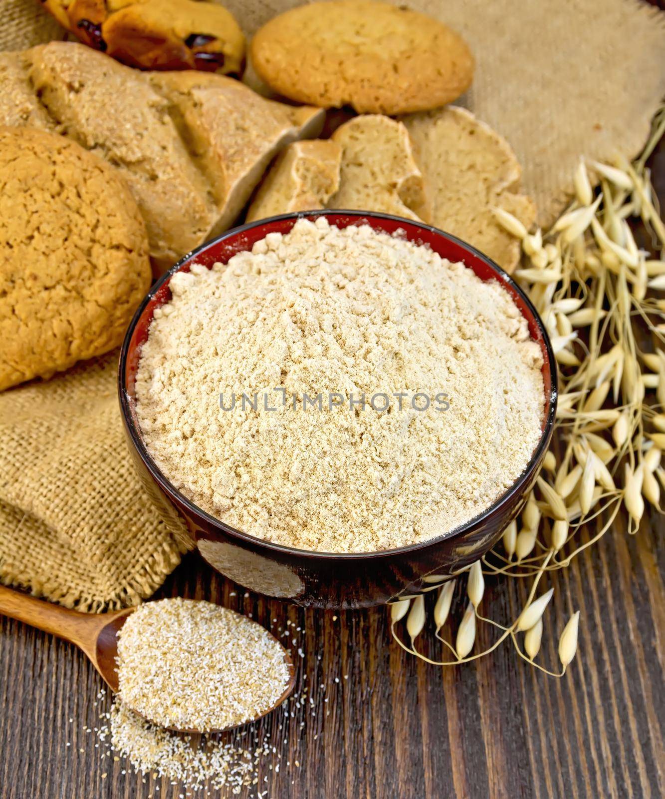Oat flour in a bowl, bag with oat and stalks of oats, biscuits and bread, oatmeal on the background of wooden boards