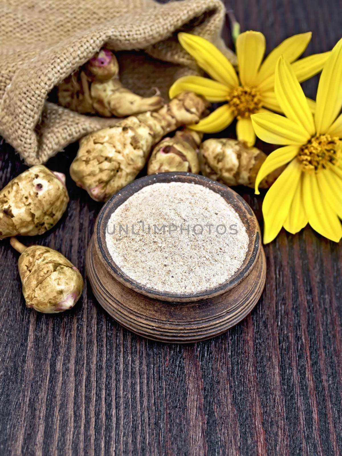 Flour of Jerusalem artichoke in a clay bowl with a flower and vegetables on a dark wooden board