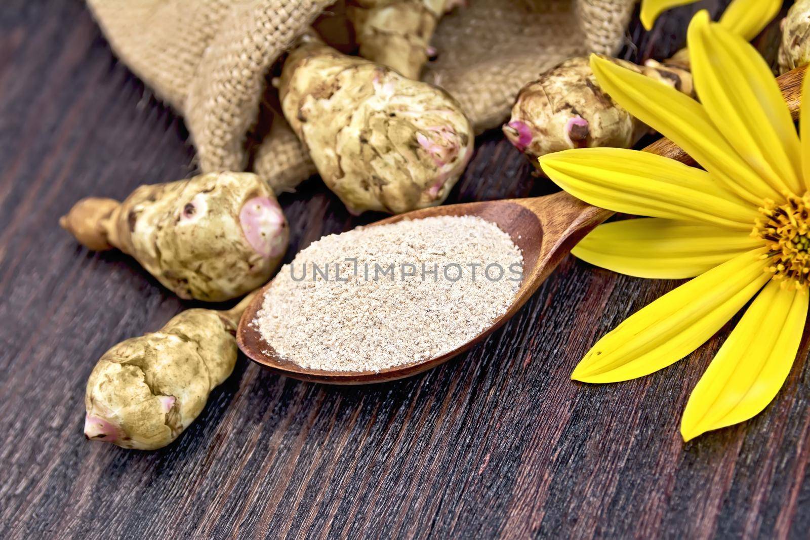 Flour of Jerusalem artichoke in a spoonful with flowers and vegetables in a bag and table against the background of wooden boards