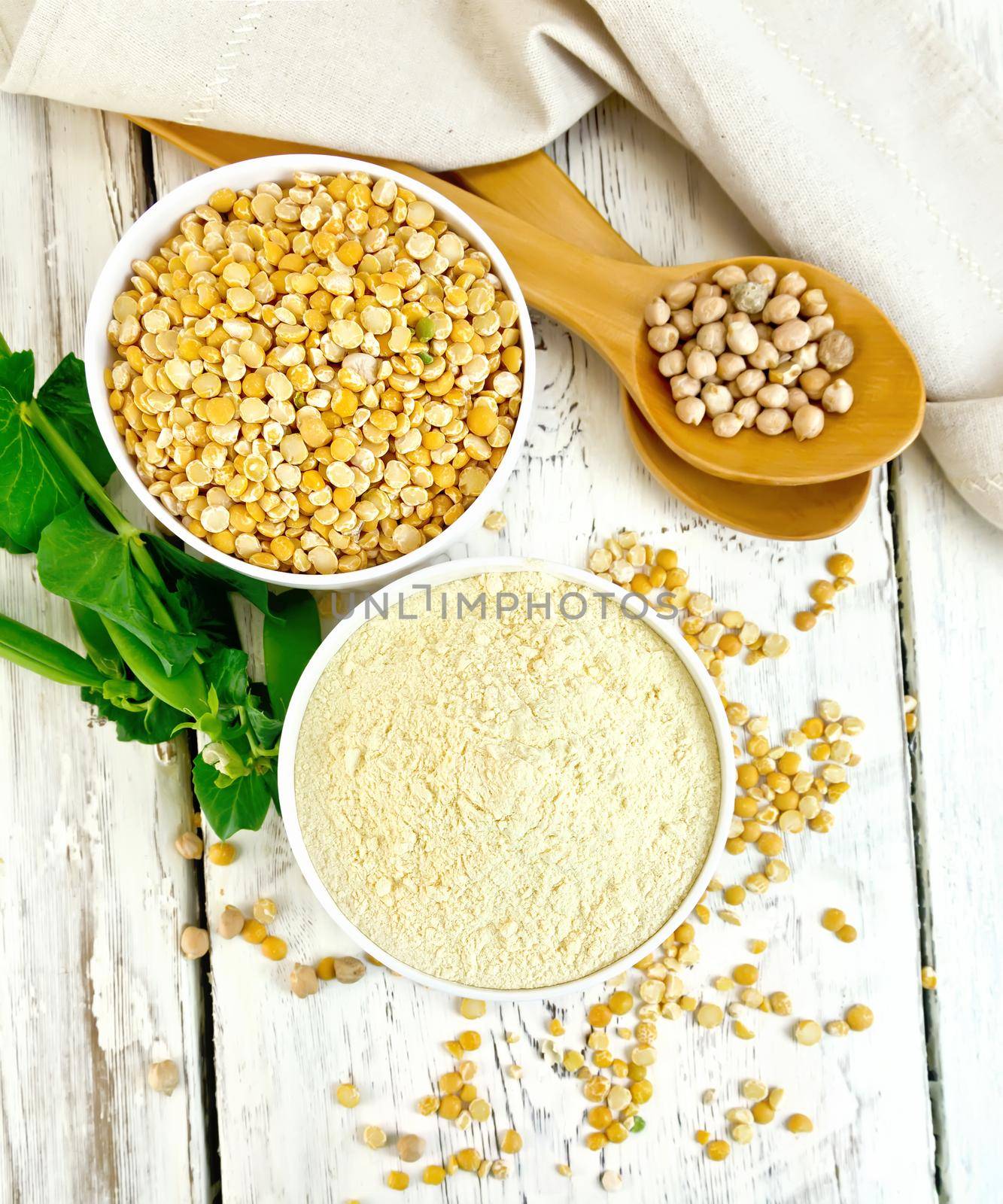 Flour pea and split pease in two white bowls, fresh pods and whole dry beans in the spoon on a background of the wooden planks on top