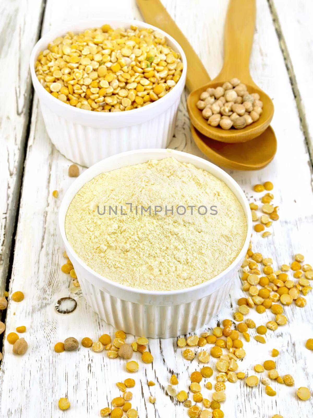 Flour pea and split pease in two white bowls, whole dry beans in the spoon on a background of light wooden planks