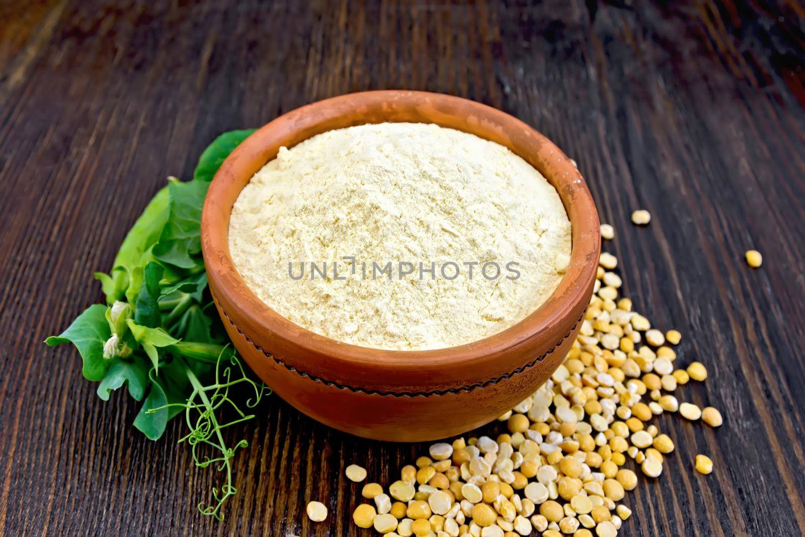 Flour pea in a clay bowl, flakes and fresh pods on a background of dark wooden boards