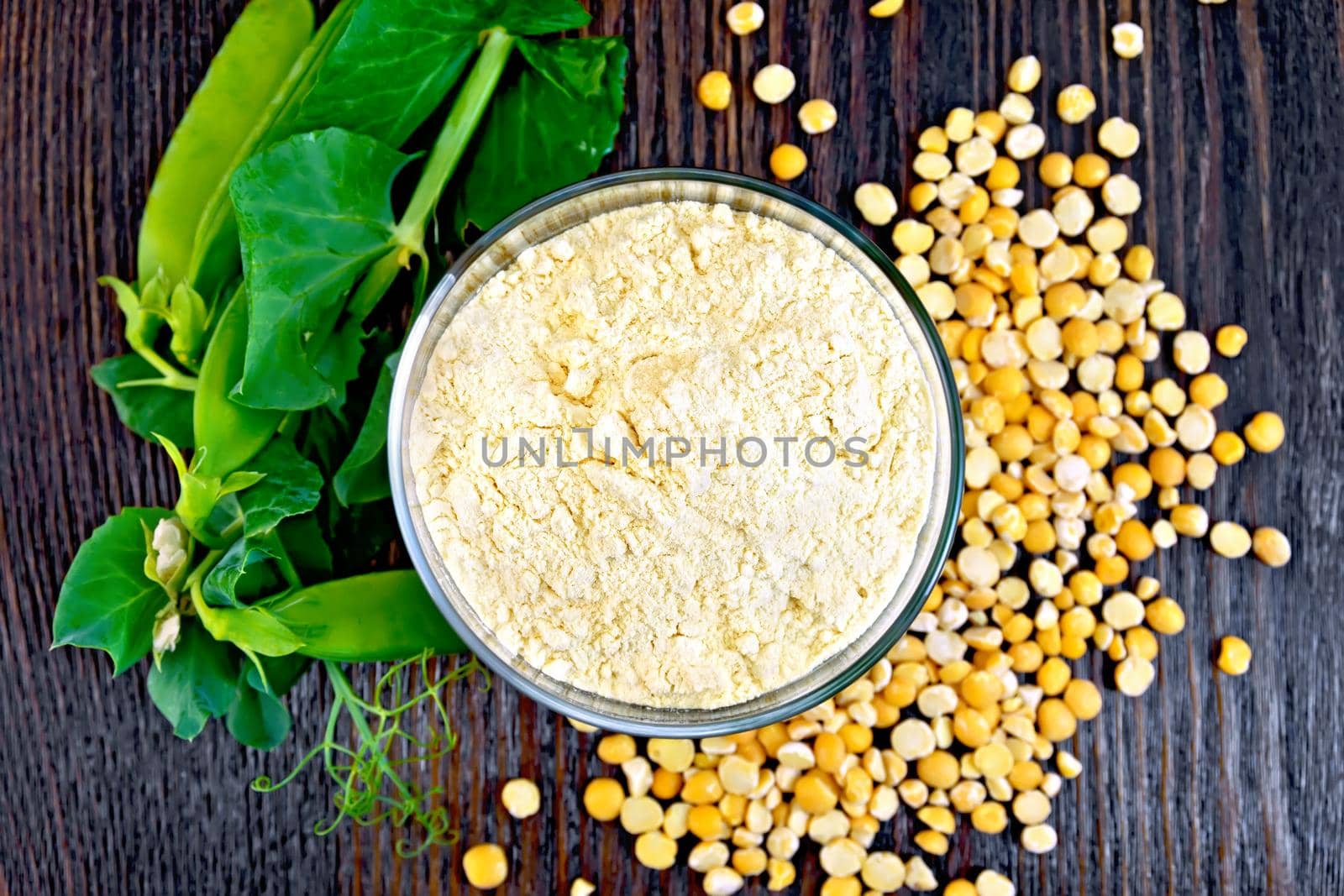 Flour pea in a glassful, fresh pods and split pease on a wooden boards background on top