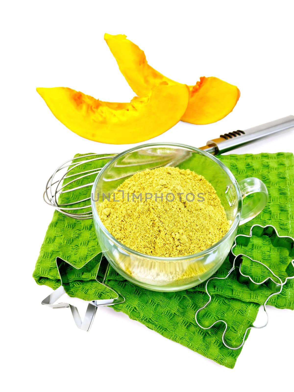 Flour pumpkin in a glass cup, mixer, cookie cutters on a green napkin, two slices of vegetables isolated on white background