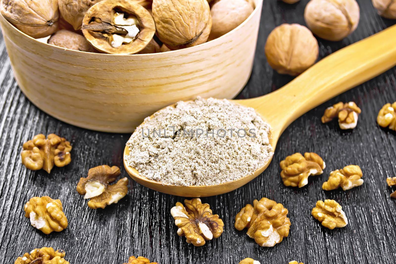 Walnut flour in a spoon, nuts in bowl and on table on background of wooden board