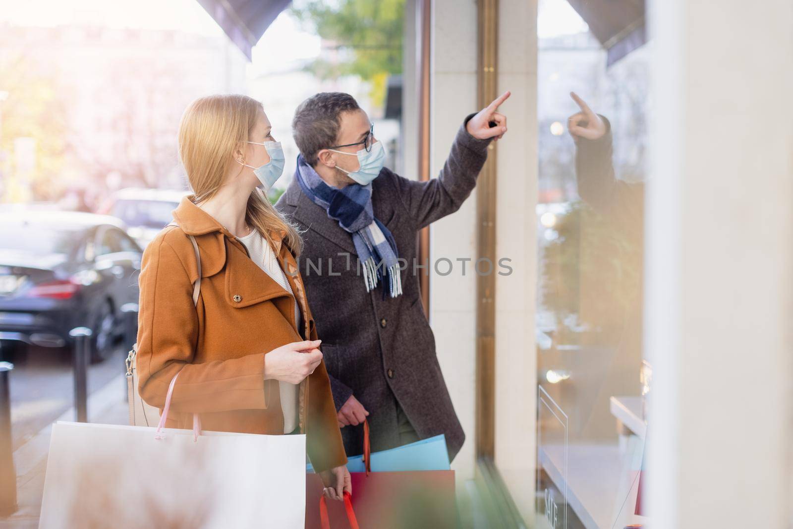 Couple doing shopping during partial lockdown standing in front of shop window with mask