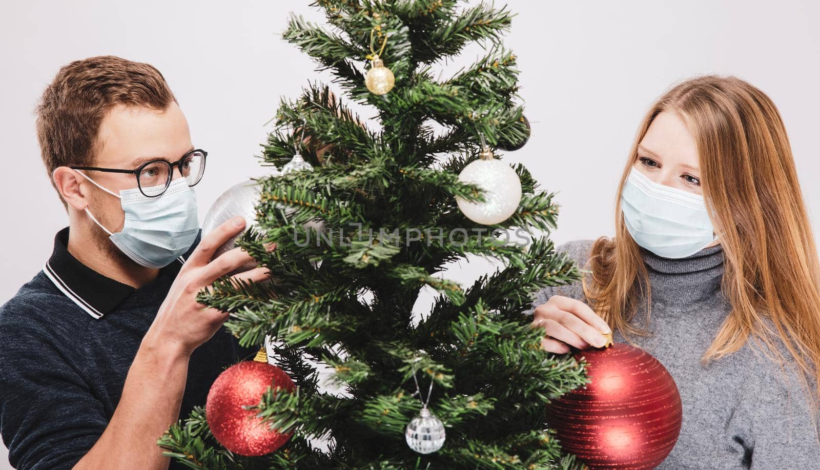 Couple decorating the Christmas tree with ornaments wearing covid-19 face mask