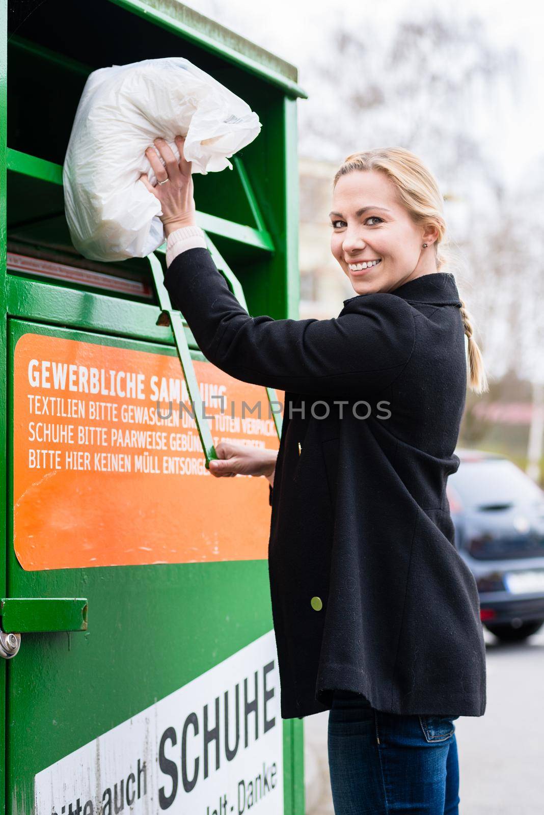 Young woman putting old or used clothes into donation bin