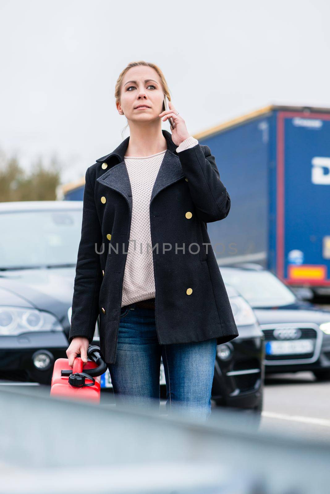 Woman out of gas car with spare canister in hand phoning for somebody to pick her up