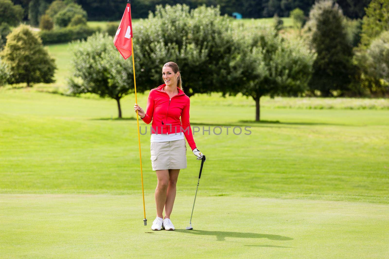 Portrait of smiling female golfer holding golf flag and club on golf green