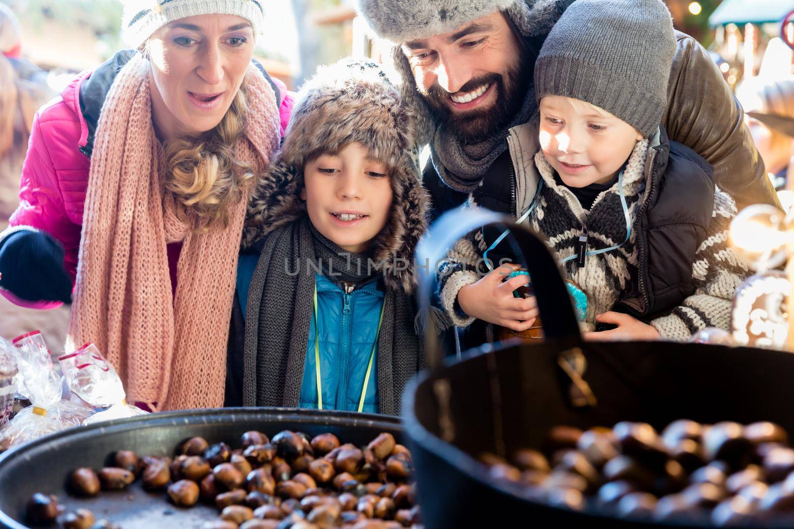 Family with two kids on Christmas market eating sweet roasted chestnuts